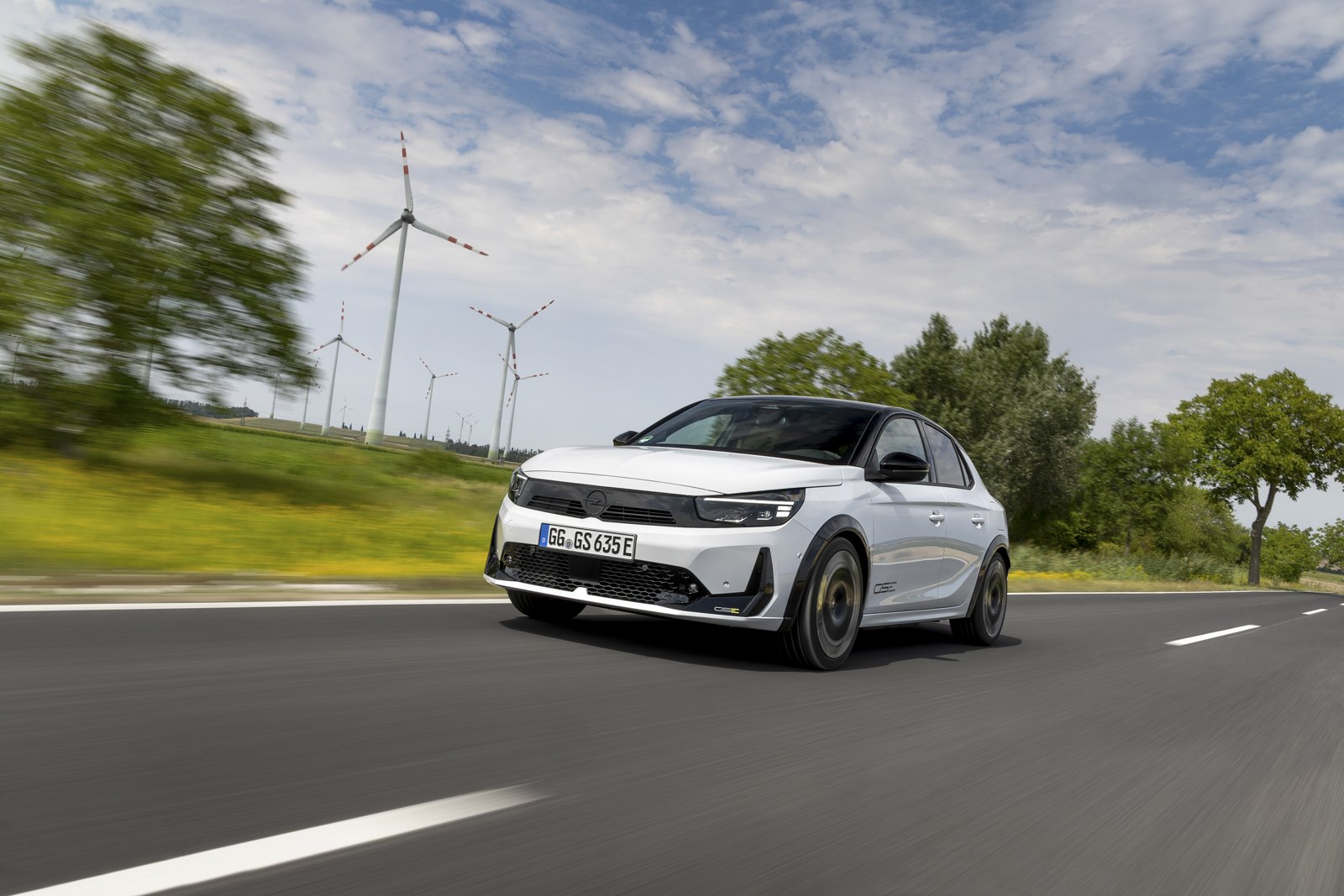 Rüzgâr türbinlerinin yanındaki yolda beyaz Opel Corsa GSE